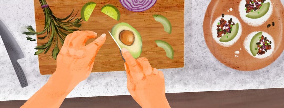 A pair of hands are slicing an avocado on a bamboo cutting board. There is a a round wooden serving plate with tacos to the right.